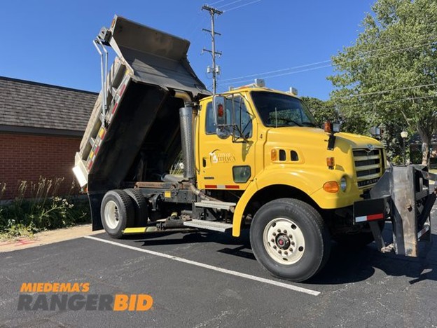 Yellow dump truck with raised bed in parking lot.