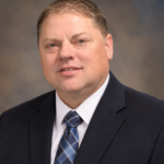 Professional headshot of man in suit and blue tie